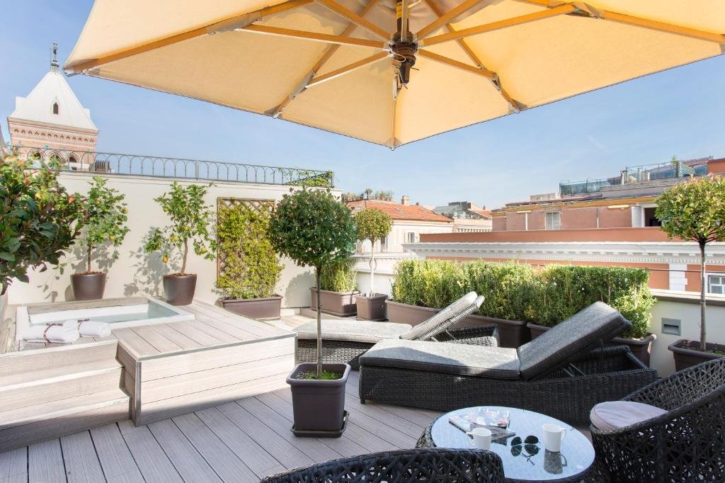 terraço de uma suíte no Hotel Artemide com banheira de hidro, duas poltronas e espreguiçadeiras e vista para a cidade e plantinhas ao redor