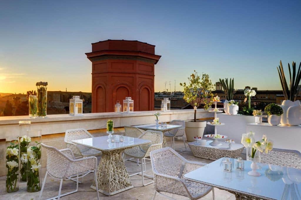 terraço do Palazzo Montemartini Rome, A Radisson Collection Hotel, com vista direta para uma bela torre, há diversas mesas e cadeiras brancos e trançadas, com plantinhas ao redor