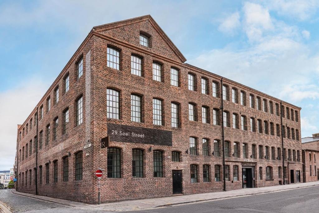 Prédio do The Resident, um dos hotéis em Liverpool, com paredes de tijolinhos, mitas janelas e céu azulado com algumas nuvens