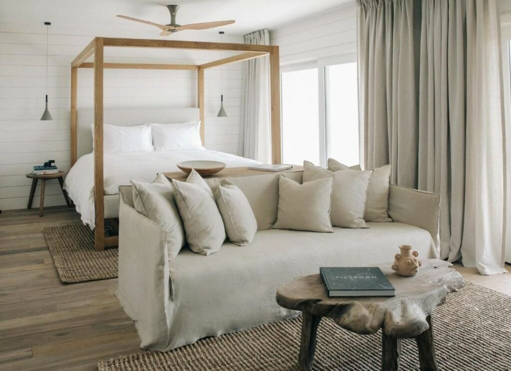 Quarto do The Surfrider Malibu. Uma mesa de centro e um sofá na frente. Atrás uma cama de casal, com um ventilador de teto e duas luminárias. Do lado direito janelas e cortinas.