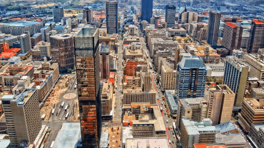 Vista aérea de 
Joanesburgo  com vários arranha-céus, edifícios urbanos e estradas sob um céu limpo.