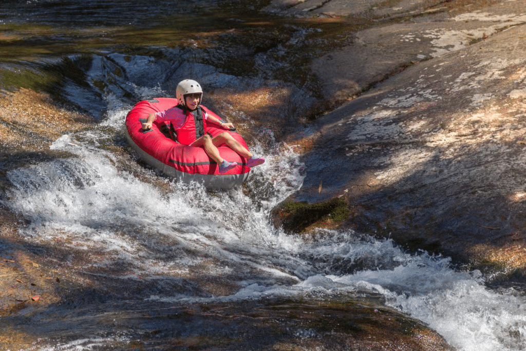 Uma pessoa usando capacete e colete salva-vidas desce um rio rochoso e raso em uma bóia inflável vermelha no rio das Almas.