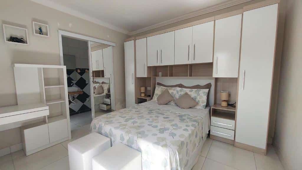 Quarto do Ubatubasul. Uma cama de casal no meio, ao redor guarda-roupa. Na frente dois puffs. No lado esquerdo mais prateleiras e a porta do banheiro com espelho. Foto para ilustrar post sobre airbnb em Perequê Mirim.