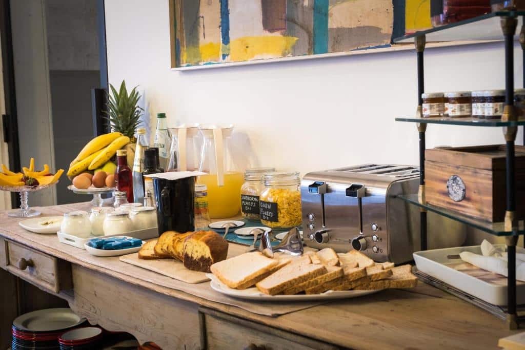 Mesa de café da manhã do Vico dei Bolognesi Palazzo Personè com pães, bolos, frutas e sucos, e uma torradeira, ilustrando post Hotéis em Puglia.