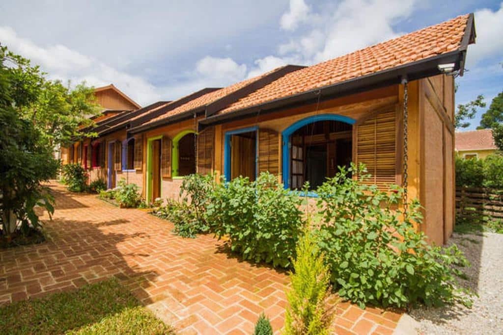 Chalés da Vila Báltica Chalés com janelas coloridas, com flores na frente, com um terraço de pedra na frente das hospedagens, onde ficar em Campos do Jordão