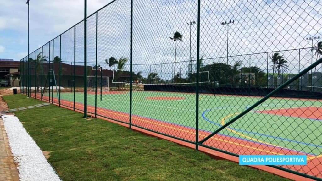 Quadra poliesportiva ao ar livre na Vila Galé Resort Alagoas - All Inclusive com superfícies vermelhas e verdes, cercada por uma cerca de arame, com palmeiras ao fundo.