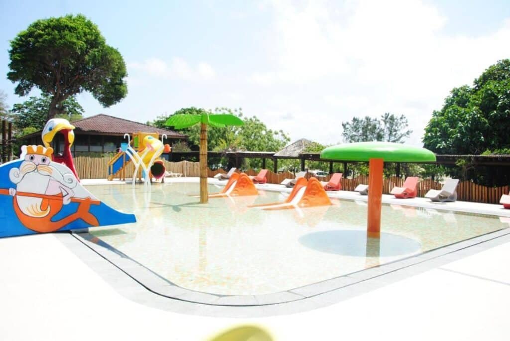 Piscina infantil com toboáguas coloridos e brinquedos aquáticos em formato de criaturas marinhas, cercada por árvores e espreguiçadeiras na Vila Galé Resort Marés - All Inclusive.