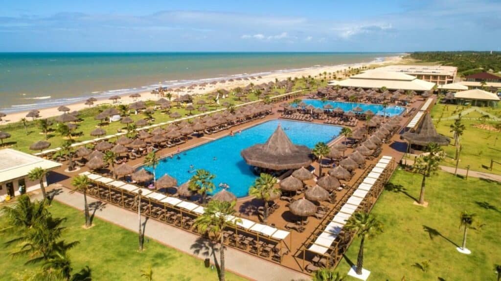 Vista aérea da Vila Galé Resort Touros à beira-mar com duas grandes piscinas, vários guarda-sóis e arredores verdejantes.