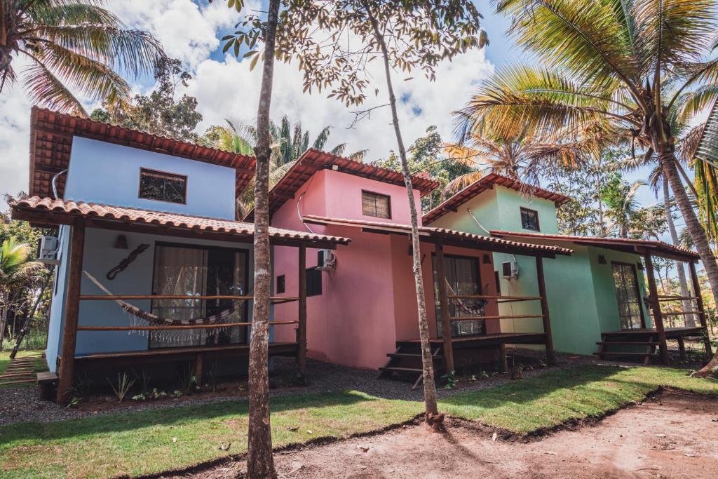 Foto de três chalés da Vila Piê. O primeiro é azul, o segundo rosa e o terceiro verde. Há árvores em volta.