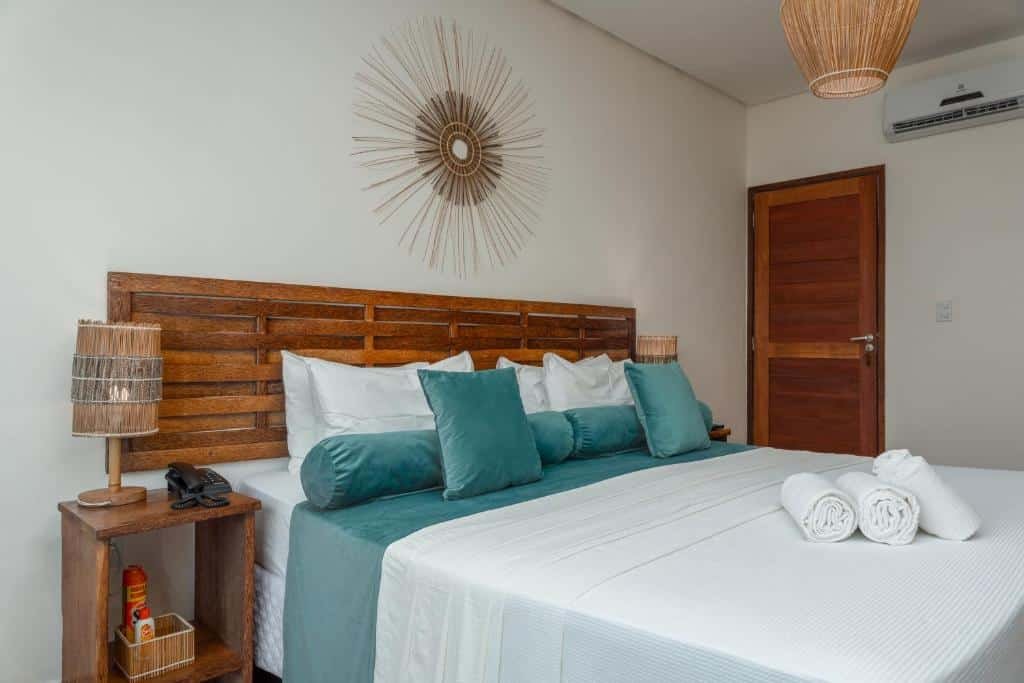 Cama de casal ampla no quarto de das alternativas às pousadas em São Miguel dos Milagres, a Villa Pantai Milagres Exclusive Hotel, com roupa de cama branca, detalhes em turquesa escuro, mesinha de cabeceira e ar-condicionado