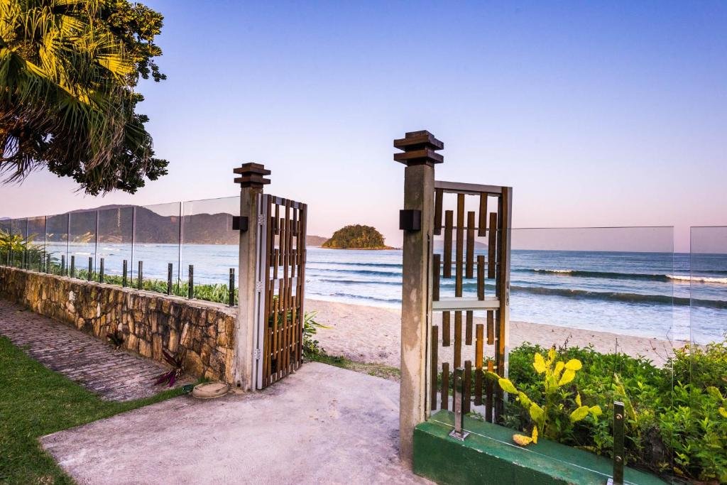 Portões da Villa Sapê Pousada abertos e com entrada direta para a faixa de areia da praia. O mar está ao fundo.