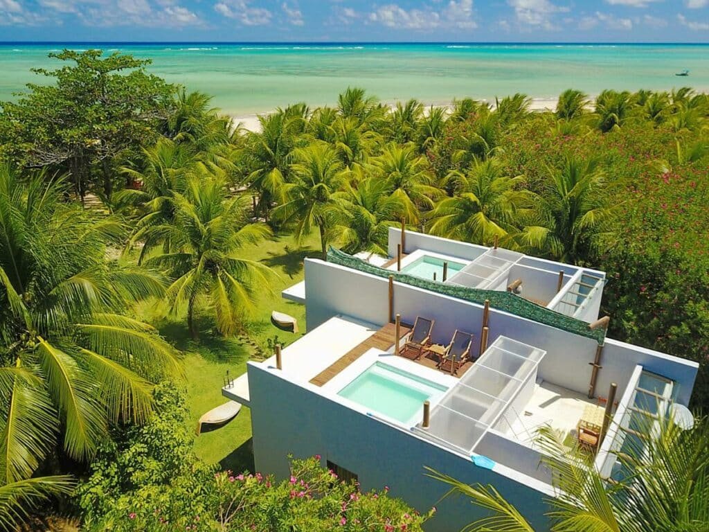 Vista das vilas no Villas Tatuté, com piscina privativa no terraço, árvores verdinhas ao redor, e ao fundo já se vê a orla branca e o mar verde translúcido de Milagres