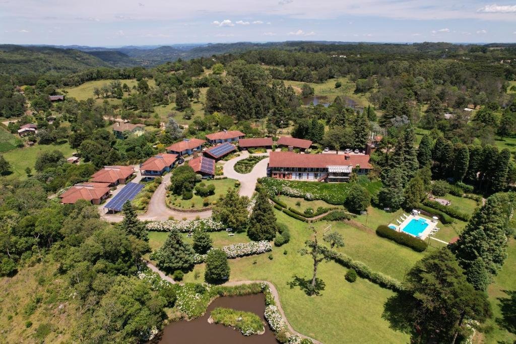 Vista de cima do Hotel Bangalôs da Serra durante o dia com mato e árvores em volta do lado direito a piscina e do lado esquerdo a propriedade.