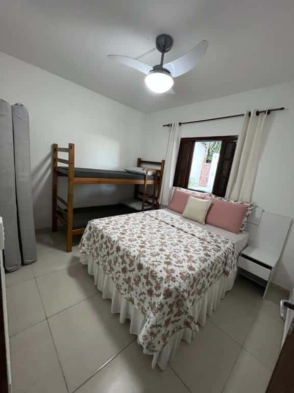 Quarto da Vista pro mar. Uma cama de casal no meio com uma prateleira do lado, em cima a janela. Do lado esquerdo no fundo uma cama de beliche, na frente dois colchões em pé. Foto para ilustrar post sobre airbnb em Perequê Mirim.