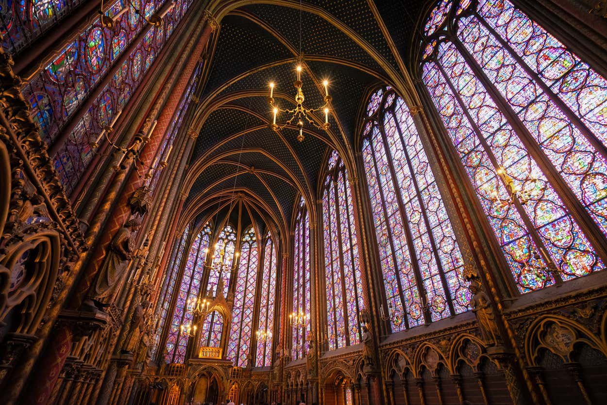 Interior ornamentado da capela gótica com altos vitrais, teto abobadado, lustres e detalhes arquitetônicos complexos. Esse é um dos pontos turísticos de Paris.